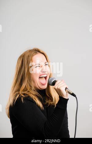 Singing my lungs out. a mature woman standing alone in the studio and using a microphone to sing karaoke. Stock Photo