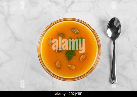 Pumpkin soup with pumpkin seeds and herbs in glass bowl on marble background Stock Photo