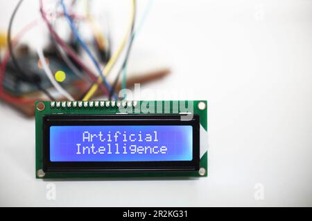Blue LCD display showing the words 'Artificial Intelligence'.  Wires from the display are connected to a circuit board in the background. Stock Photo