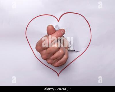 Close-up of a hand with the Korean heart symbol with forefinger and thumb, after punching a white paper with a red heart drawn Stock Photo