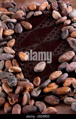 Dark chocolate tablet accompanied with roasted cocoa beans. Studio photo on brown background with stucco texture. Vintage rustic air. Stock Photo