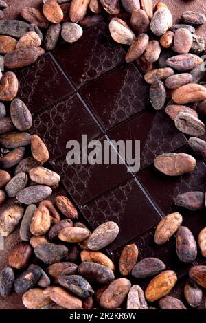 Dark chocolate tablet accompanied with roasted cocoa beans. Studio photo on brown background with stucco texture. Vintage rustic air. Stock Photo