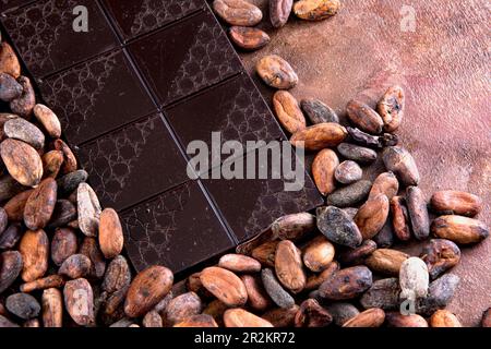 Dark chocolate tablet accompanied with roasted cocoa beans. Studio photo on brown background with stucco texture. Vintage rustic air. Stock Photo