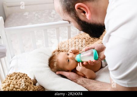 Boy feeding milk to brother from baby bottle while sitting on sofa at home  Stock Photo - Alamy