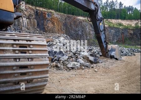 Excavator bucket at basalt quarry. Basalt mining. Excavators in a basalt quarry near the forest. Large excavator in an outdoor mine Stock Photo