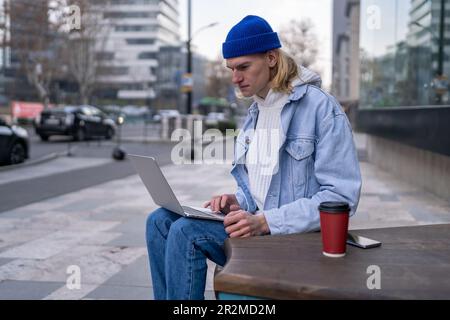 Focused busy guy freelancer works on laptop sits on bench on street in city downtown.  Stock Photo