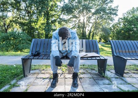 Young sad sick poor homeless man sitting on the street need help feeling lonely and depressed because he is abandoned from family and friends when he Stock Photo