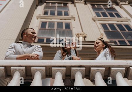 Three best friends leaning on the fence while talking and standing in front of the building Stock Photo