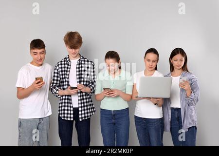 Group of happy teenagers using different gadgets on light grey background Stock Photo