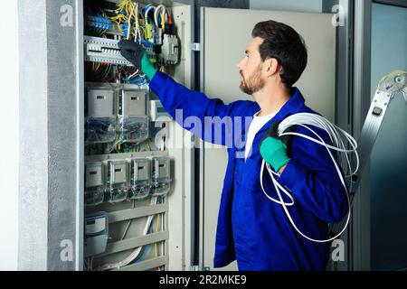 Electrician with wires switching off circuit breakers in fuse box indoors Stock Photo