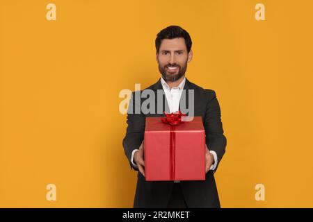 Handsome man holding gift box on yellow background Stock Photo