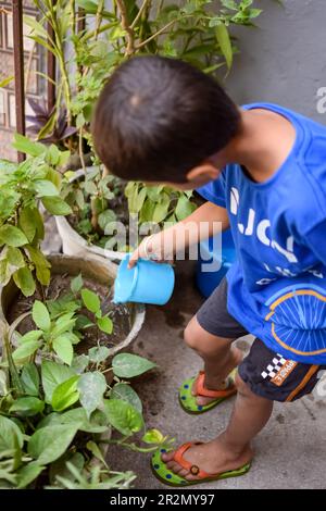 Cute 5 year’s old Asian little boy is watering the plant in the pots located at house balcony. Love of sweet little boy for the mother nature during w Stock Photo