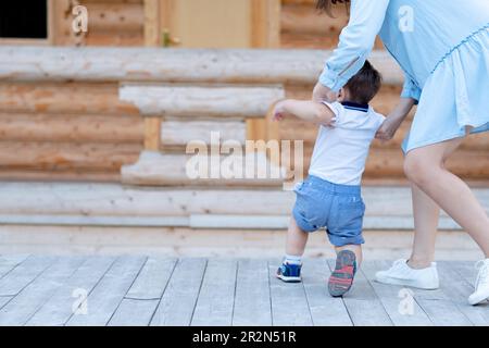 the boy learns to walk and takes his first steps with his mother. Baby and his first steps. Mother's support for the child Stock Photo