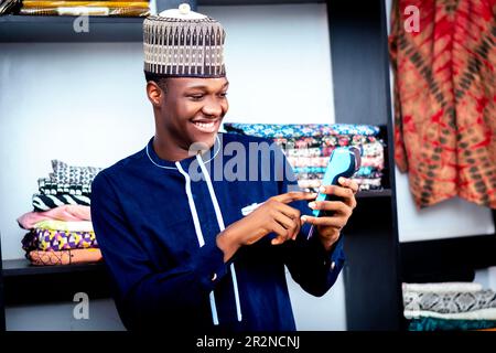 Photo of a black african man in a blue shirt typing code on a pos machine while standing Stock Photo