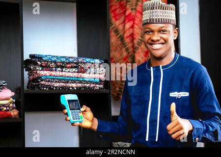 Photo of a black african man showing approval with a thumbs up while holding pos machine Stock Photo