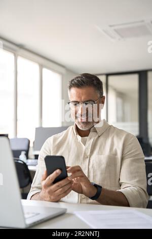 Vertical portrait of middle aged Hispanic business using cell phone mobile app. Stock Photo