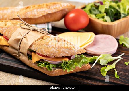 fresh submarine sandwich with ham, cheese, bacon, tomatoes, lettuce, on wooden cutting board Stock Photo