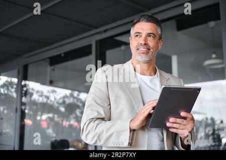 Smiling mid aged business man standing outside office holding digital tablet. Stock Photo