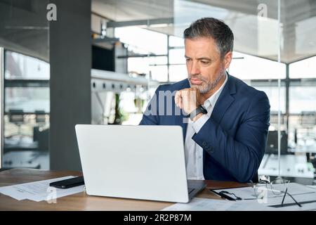 Busy serious mature business man ceo looking at laptop analyzing financial data. Stock Photo