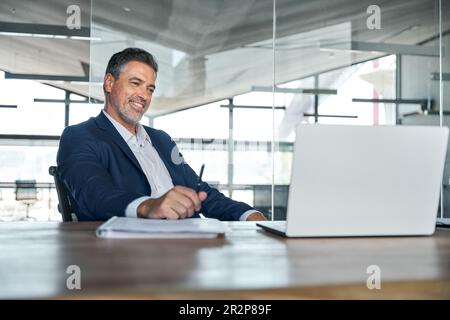 Smiling mature adult business man wearing suit looking at laptop at workplace. Stock Photo