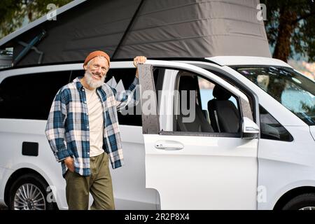 Happy older man traveler standing with camper van, campervan rentals. Stock Photo