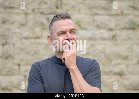 Gray-haired man standing in front of a wall and looking sideways thoughtfully Stock Photo