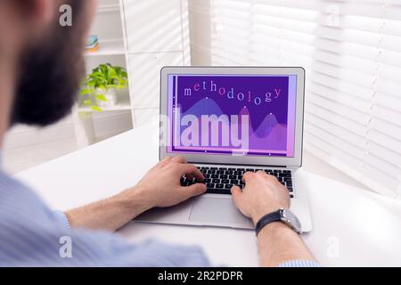 Methodology concept. Man using modern laptop at white table indoors, closeup Stock Photo