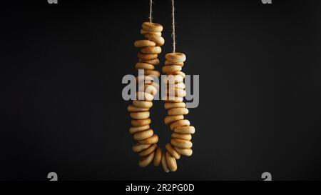 Bunch of delicious ring shaped Sushki (dry bagels) hanging on black background Stock Photo