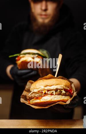 Man Black Gloves Holding Burger Hands Juicy Burger Close Appetizing burger. Stock Photo