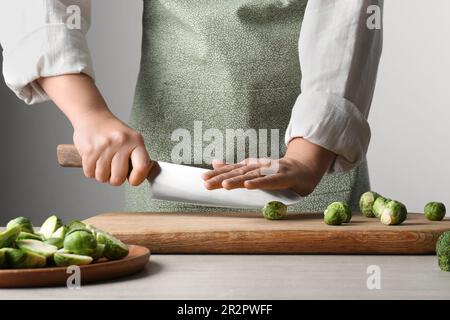 Woman cutting fresh brussel sprouts on board at wooden table, closeup Stock Photo