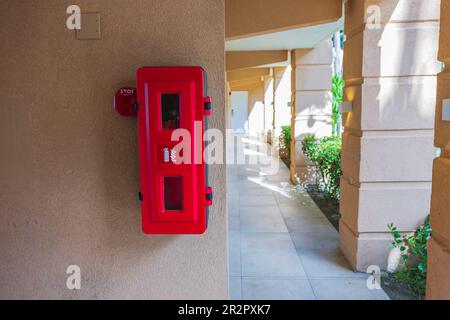View of fire extinguisher box with fire extinguisher and call button on hotel wall. Aruba. Stock Photo