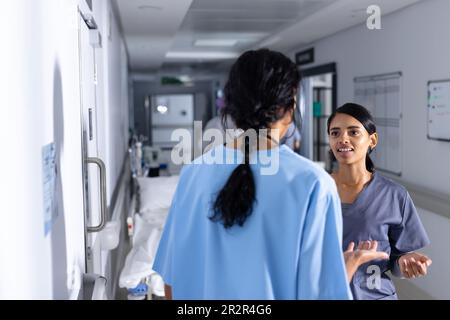 Two biracial female doctors wearing scrubs, talking in corridor at hospital Stock Photo