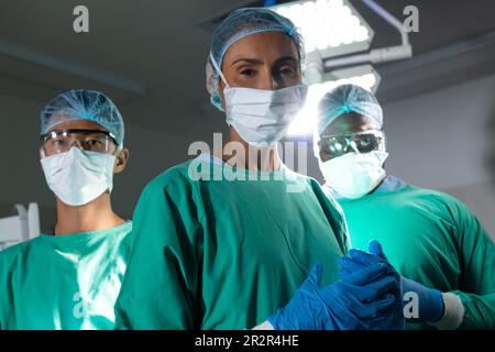 Portrait of biracial male surgeon in surgical cap and mask in operating ...