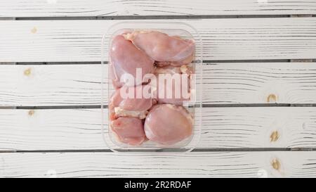 Raw skinless boneless chicken thighs in plastic container close-up on white wooden board, flat lay with copy space Stock Photo