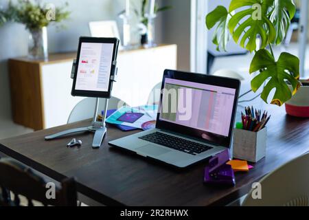 Laptop and tablet, with spreadsheet and document on screen, on dining table in home office. Remote working, communication, technology, business and mo Stock Photo