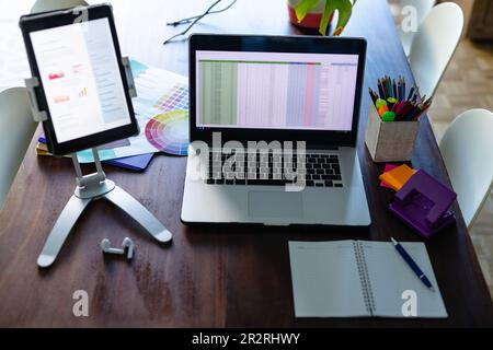 Notepad, laptop and tablet with spreadsheet and document on screen, on dining table in home office. Remote working, communication, technology, busines Stock Photo