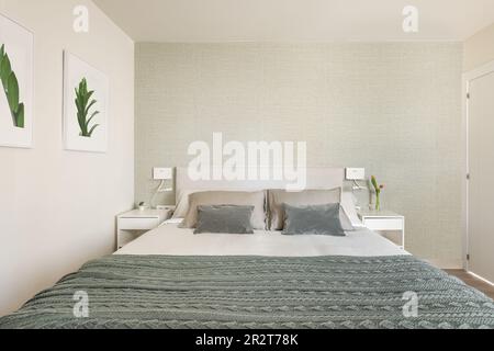 Stylish bright bedroom with bedside tables and a double bed with green beige wallpaper and cute pictures on the wall. The concept of a small but cozy Stock Photo