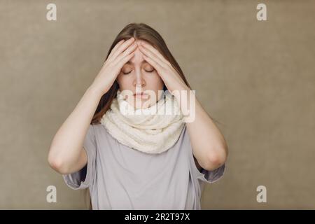 Young woman wearing scarf holds head flu catarrh ill sick disease treatment cold Stock Photo