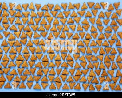 Fun flat lay of pet kibble arranged on a blue background. Triangle shaped pellets of cat or dog dry food top view Stock Photo
