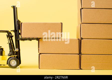 Forklift truck raises cardboard boxes on a yellow background. Cargo ...