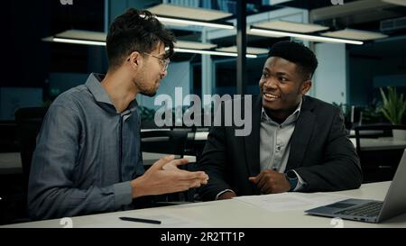 Diverse businessmen african american indian men talking discussing online project on computer sit at office desk two multiracial 30s male colleagues Stock Photo