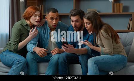 Surprised 30s middle-aged women men consumers read good news on mobile phone cellphone diverse ethnic friends multiracial people using virtual app Stock Photo