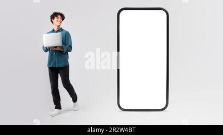 Man Using Laptop Looking At Giant Phone Screen, White Background Stock Photo