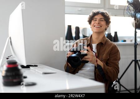 Professional photographer young man working on photo shoot at studio, holding dslr camera, using pc computer Stock Photo