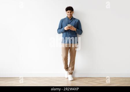 Young Arab Man Using Phone Standing Against White Studio Wall Stock Photo