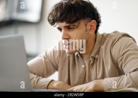 Portrait Of Tired Young Man Using Laptop Sitting In Office Stock Photo