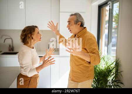 Relationship problems. Angry senior man arguing with his wife at kitchen, spouses having difficulties in marriage Stock Photo