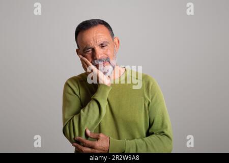 Sad caucasian aged man in casual presses his hands to cheek, suffering from toothache Stock Photo