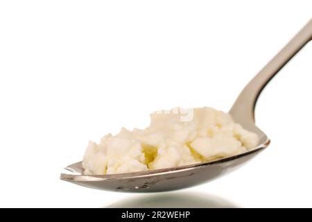 Fresh cottage cheese in a metal spoon, macro, isolated on white background. Stock Photo