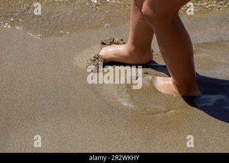 Barefoot feet of a child in the coastal sand, view from above. Summer vacation. Stock Photo